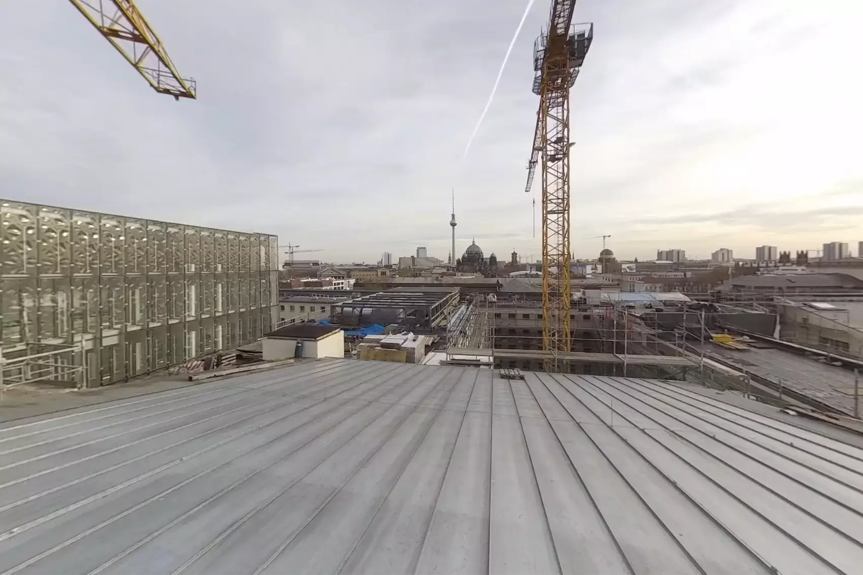 Blick über eine Dachbaustelle mit Kränen auf die Berliner Innenstadt.