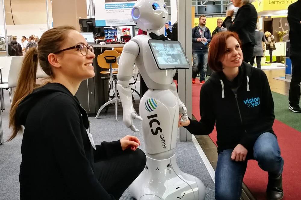 Die Gründerinnen von visionYOU neben dem humanoiden Roboter Pepper auf einer Bildungsmesse.