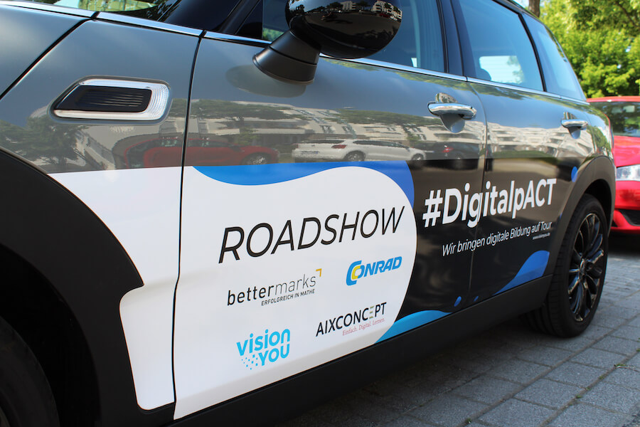 Seitliche Ansicht eines grauen Autos mit Folierung zur Roadshow #DigitalpACT mit Logos der beteiligten Partner.