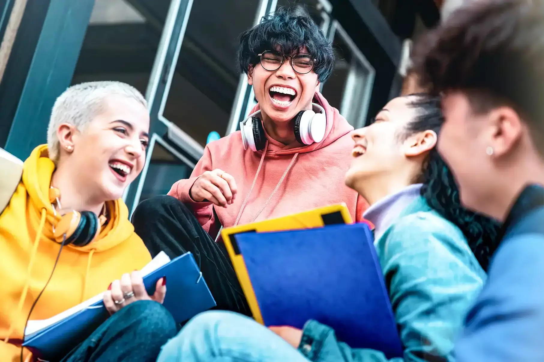 Vier junge Menschen sitzen mit Notizbüchern zusammen und lachen.