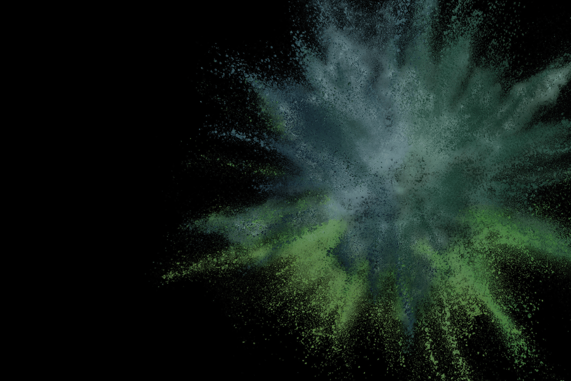 Explosion aus grünem und blauem Farbpulver vor schwarzem Hintergrund.