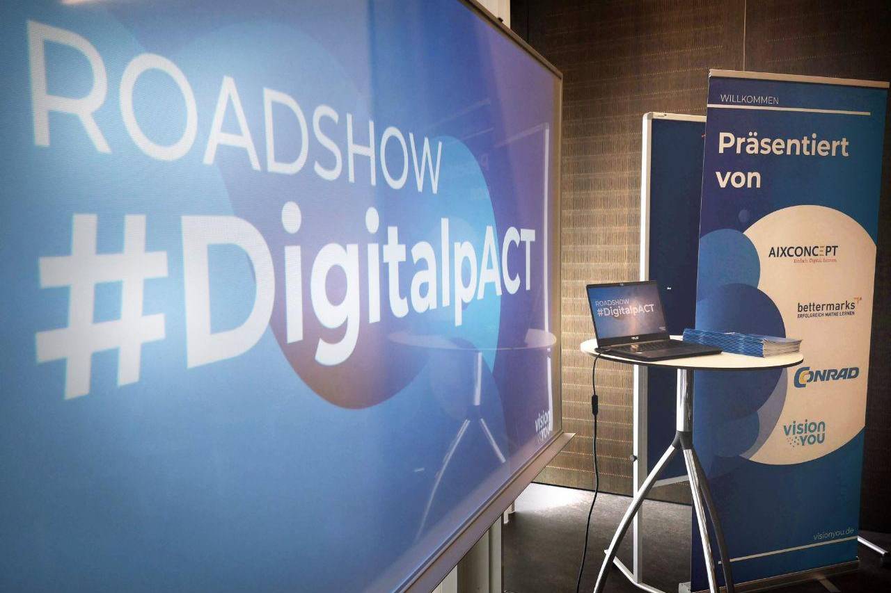 Veranstaltungsaufbau der Roadshow #DigitalpACT mit Bildschirm, Laptop und Sponsorenbanner.