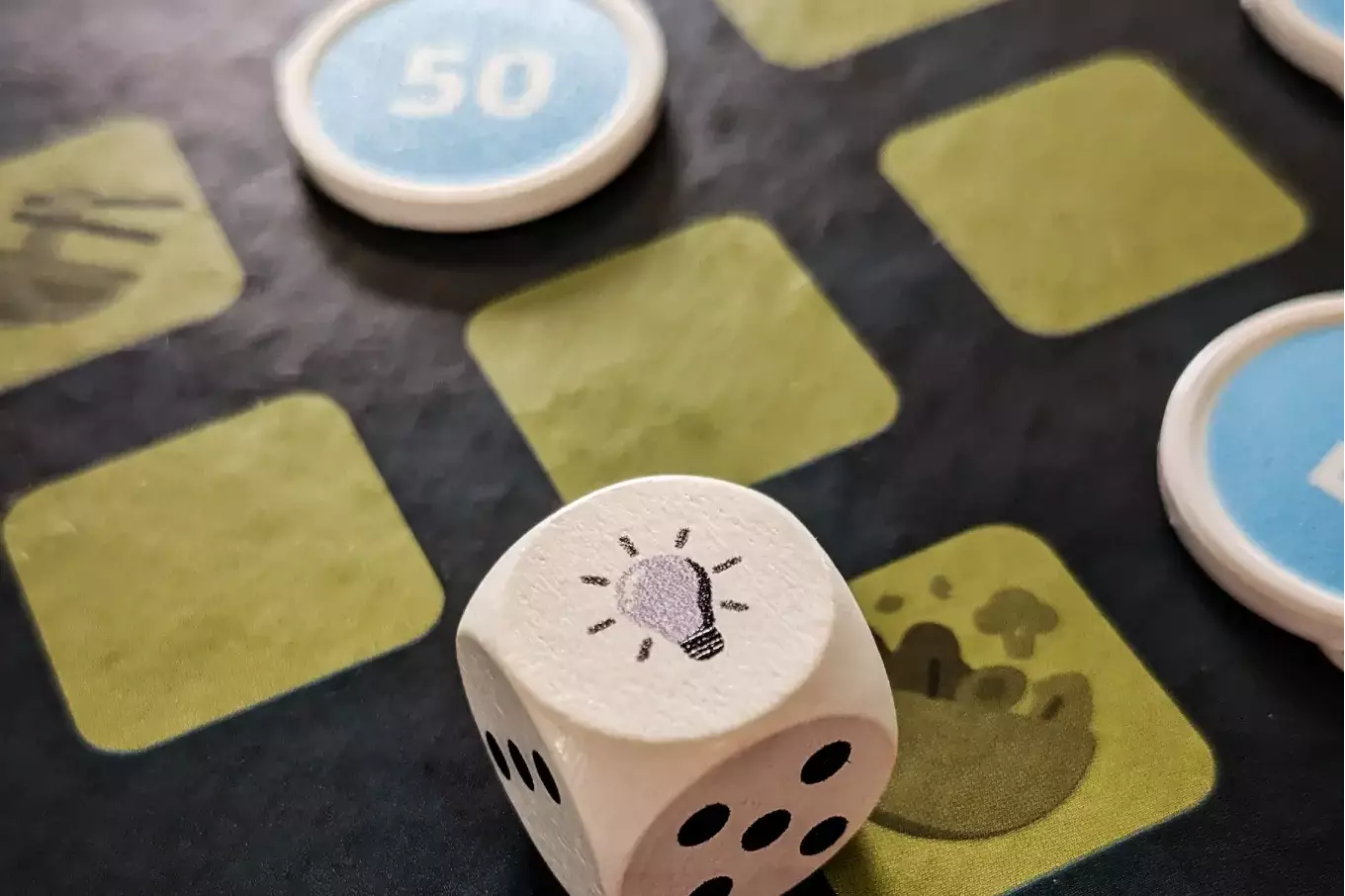 Holzwürfel mit Glühbirnen-Symbol auf dem Spielplan von „Vision Mensa“.