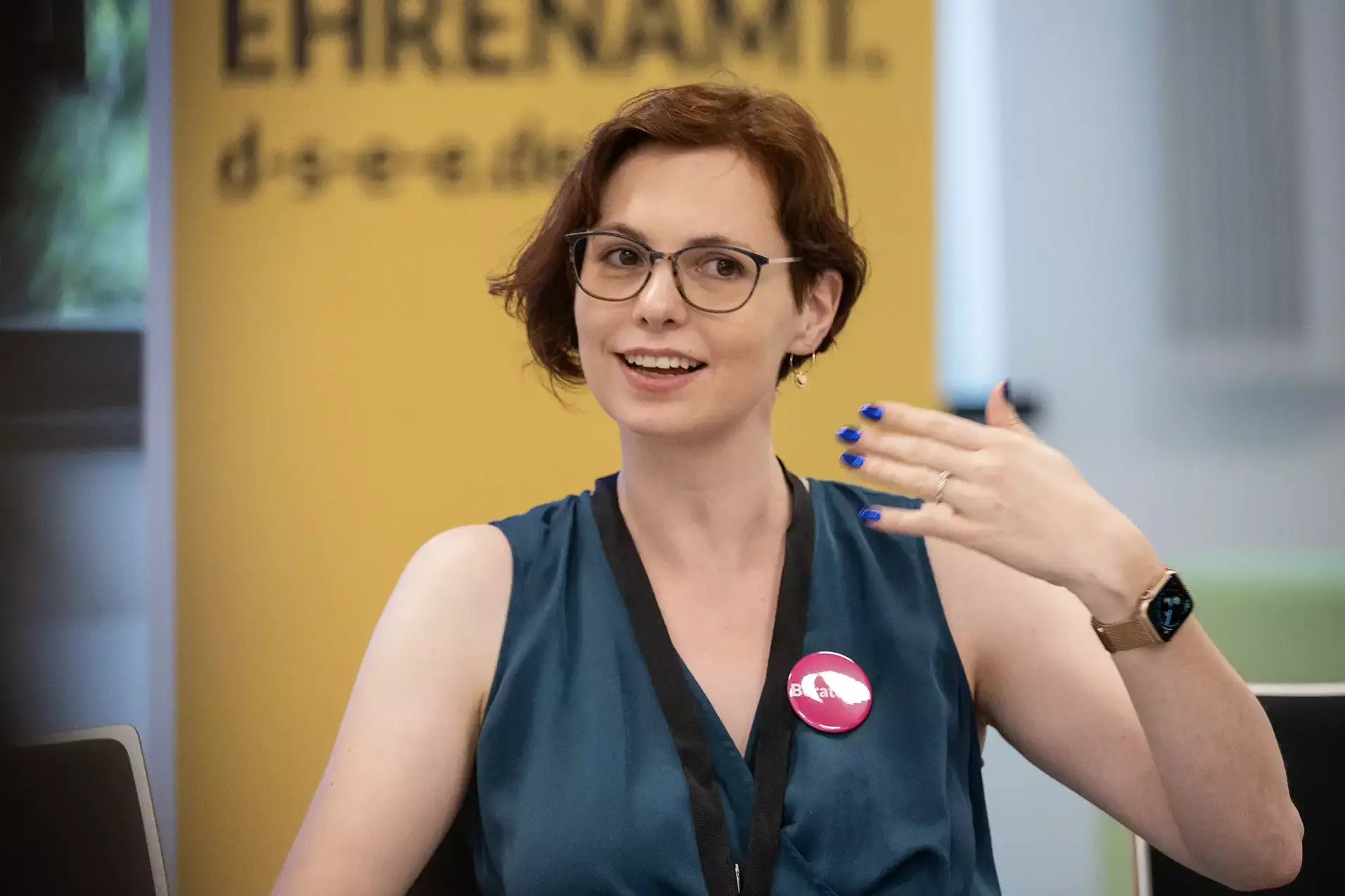 Beraterin mit Brille spricht und gestikuliert während einer Veranstaltung.